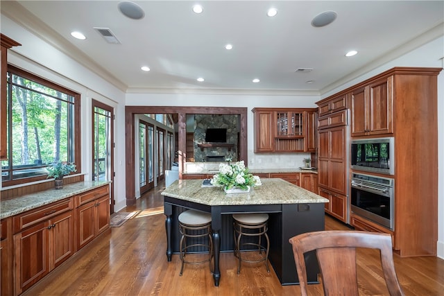 kitchen featuring a kitchen breakfast bar, a kitchen island, black microwave, stainless steel oven, and hardwood / wood-style floors