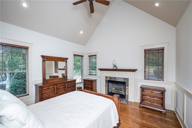 bedroom with ceiling fan, dark wood-type flooring, high vaulted ceiling, and a tile fireplace