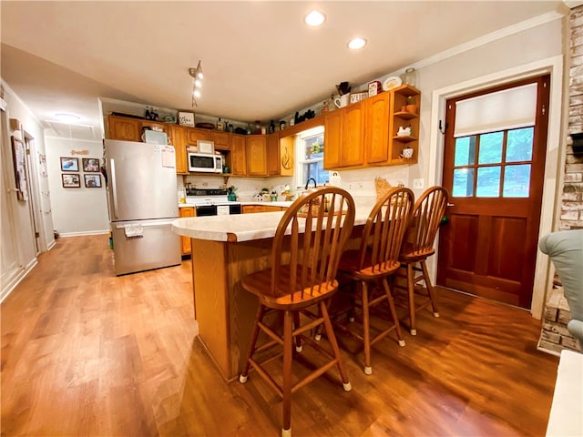 kitchen with kitchen peninsula, white appliances, a breakfast bar area, crown molding, and light hardwood / wood-style floors