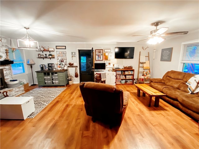 living room with a stone fireplace, ceiling fan with notable chandelier, hardwood / wood-style floors, and a wealth of natural light