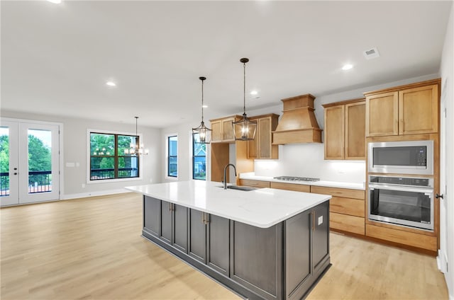 kitchen with a center island with sink, appliances with stainless steel finishes, hanging light fixtures, and premium range hood