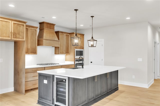 kitchen featuring pendant lighting, an island with sink, beverage cooler, light hardwood / wood-style flooring, and premium range hood