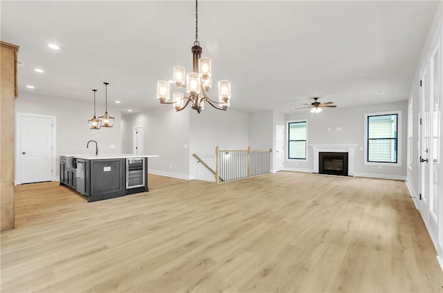 kitchen with ceiling fan, pendant lighting, wine cooler, an island with sink, and light wood-type flooring