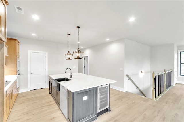 kitchen with light wood-type flooring, sink, pendant lighting, and an island with sink