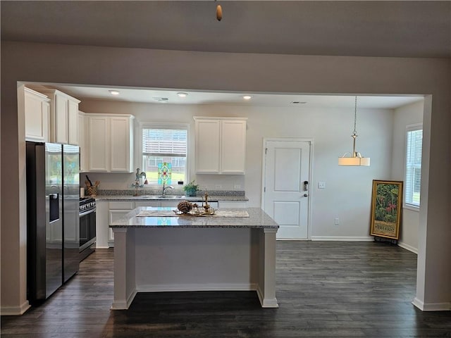 kitchen with a center island, dark wood-type flooring, white cabinets, light stone countertops, and appliances with stainless steel finishes