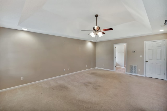 empty room with a raised ceiling, ceiling fan, and light colored carpet