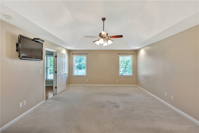 carpeted empty room with ceiling fan, a tray ceiling, and a wealth of natural light