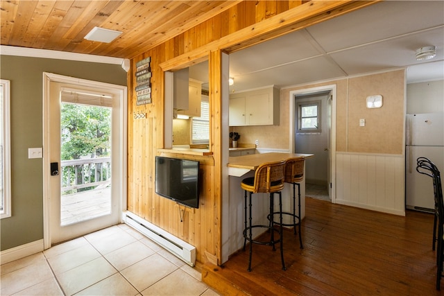 kitchen featuring light hardwood / wood-style flooring, a baseboard heating unit, white cabinetry, a kitchen breakfast bar, and white fridge