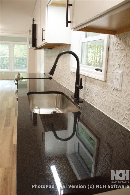 interior details featuring tasteful backsplash, dark stone countertops, sink, and white cabinets