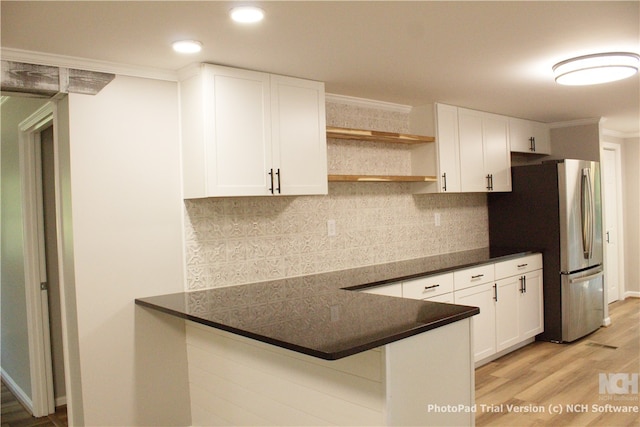 kitchen featuring a kitchen breakfast bar, kitchen peninsula, light hardwood / wood-style flooring, stainless steel fridge, and white cabinetry