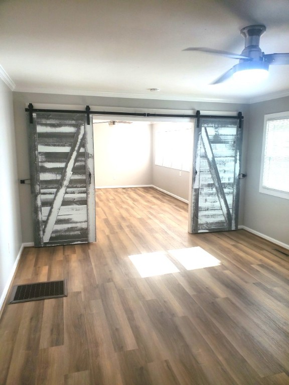 spare room featuring hardwood / wood-style floors, ceiling fan, a barn door, and crown molding