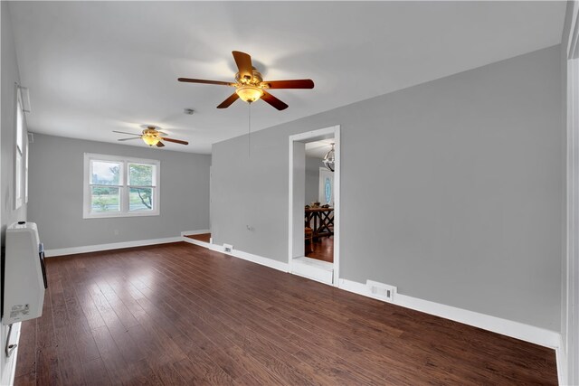 empty room featuring heating unit, ceiling fan, and dark wood-type flooring