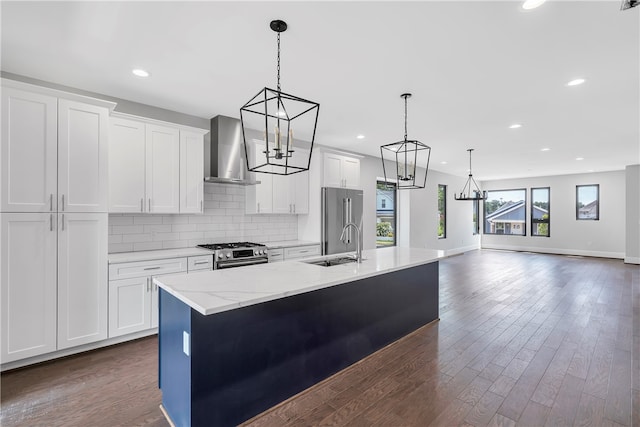 kitchen with appliances with stainless steel finishes, wall chimney exhaust hood, an island with sink, and white cabinets