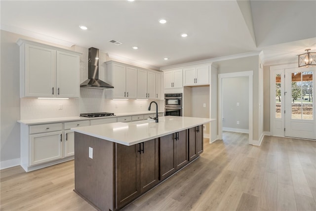 kitchen featuring light hardwood / wood-style floors, an island with sink, wall chimney exhaust hood, stainless steel appliances, and sink