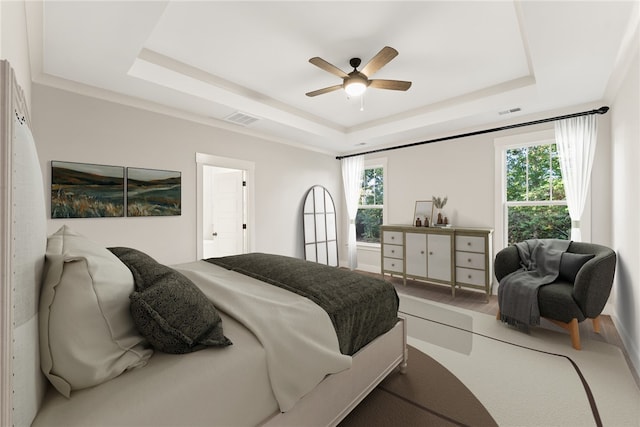 bedroom with hardwood / wood-style floors, multiple windows, a raised ceiling, and ceiling fan