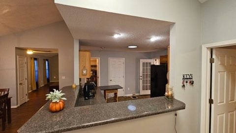 kitchen featuring kitchen peninsula, vaulted ceiling, dark hardwood / wood-style floors, and black fridge