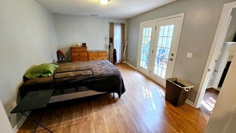 bedroom with access to outside, a textured ceiling, and hardwood / wood-style flooring