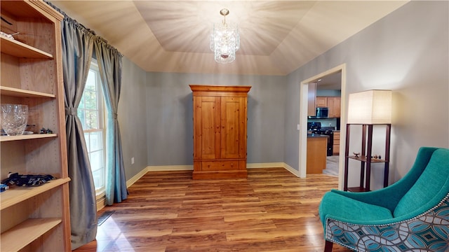 sitting room featuring a raised ceiling, vaulted ceiling, hardwood / wood-style flooring, and an inviting chandelier