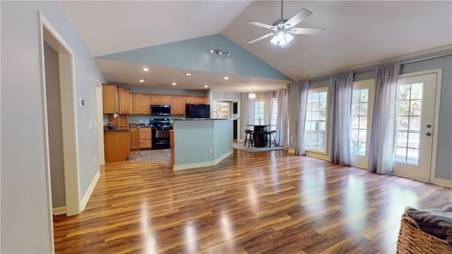 kitchen with light wood-type flooring, ceiling fan, black appliances, high vaulted ceiling, and a kitchen island