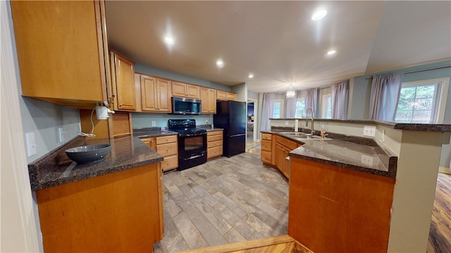 kitchen featuring a kitchen island with sink, black appliances, sink, light hardwood / wood-style flooring, and dark stone countertops