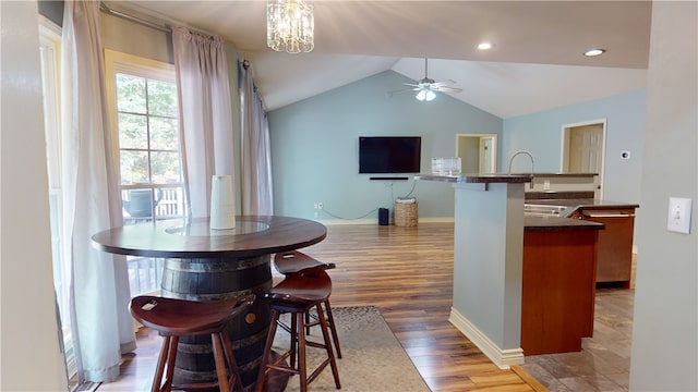 dining area with hardwood / wood-style floors, ceiling fan with notable chandelier, lofted ceiling, and sink