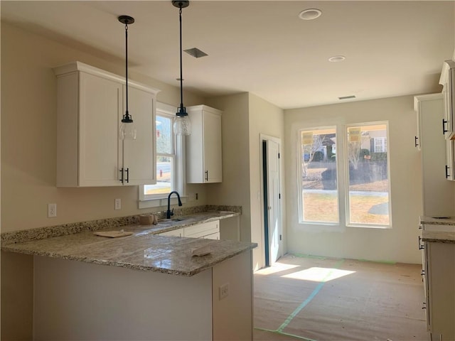 kitchen featuring sink, light stone counters, kitchen peninsula, decorative light fixtures, and white cabinets