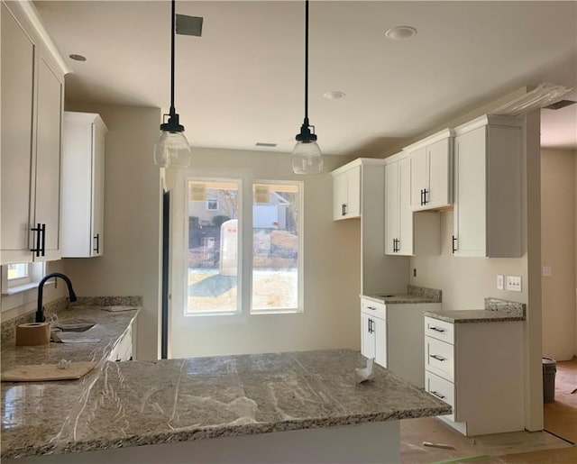 kitchen featuring stone counters, white cabinetry, hanging light fixtures, and sink