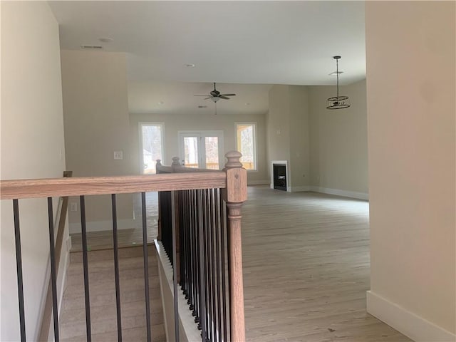 hallway with an upstairs landing, visible vents, light wood-style flooring, and baseboards