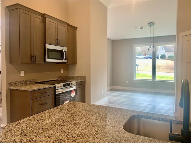 kitchen with visible vents, appliances with stainless steel finishes, decorative light fixtures, light stone countertops, and a sink