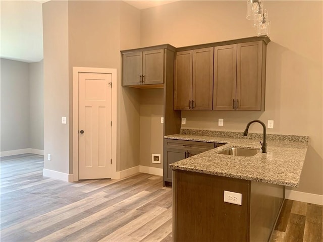 kitchen with light stone counters, light wood-style floors, a sink, and a peninsula