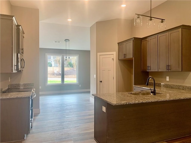 kitchen with light wood-style flooring, appliances with stainless steel finishes, a peninsula, light stone countertops, and a sink