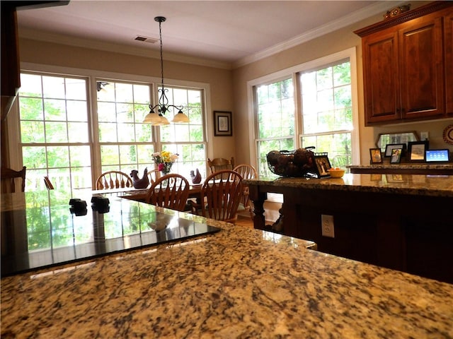 kitchen with hanging light fixtures, ornamental molding, and dark stone counters