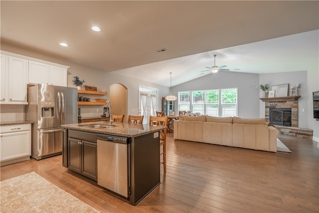 kitchen featuring sink, white cabinets, a center island with sink, appliances with stainless steel finishes, and a stone fireplace