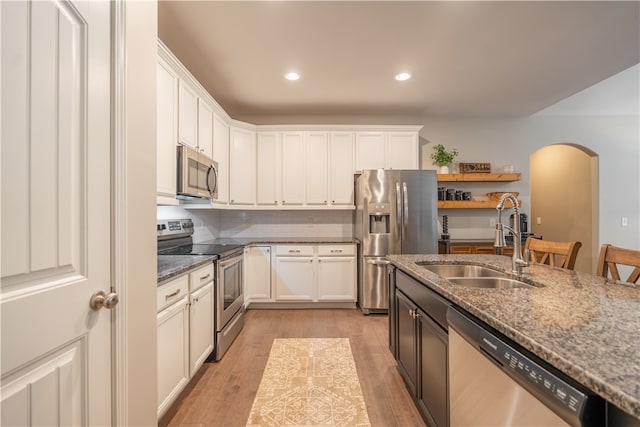 kitchen featuring sink, dark stone counters, white cabinetry, stainless steel appliances, and light wood-type flooring