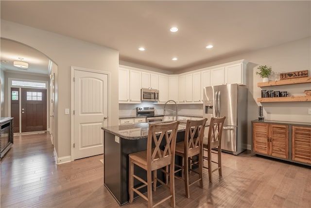 kitchen with appliances with stainless steel finishes, light hardwood / wood-style floors, a breakfast bar, white cabinets, and dark stone counters