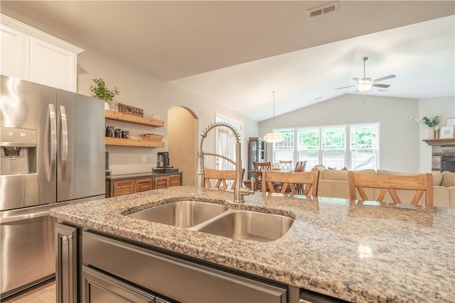 kitchen with light stone countertops, stainless steel fridge, sink, and lofted ceiling