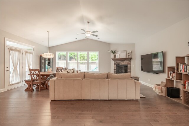 living room featuring ceiling fan with notable chandelier, a fireplace, lofted ceiling, and dark wood-type flooring