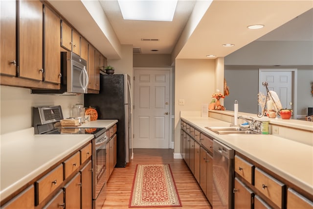 kitchen with light wood-type flooring, sink, kitchen peninsula, stainless steel appliances, and a skylight