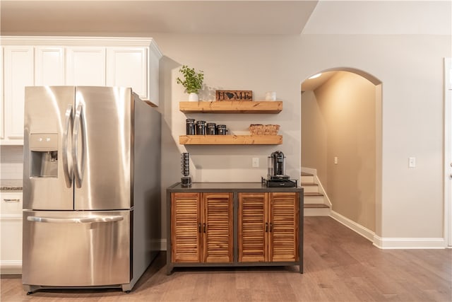 kitchen with stainless steel refrigerator with ice dispenser, light hardwood / wood-style floors, and white cabinets