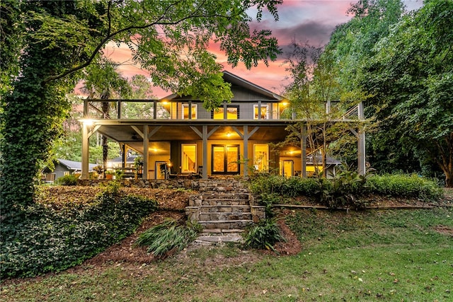 back house at dusk featuring a lawn and a porch