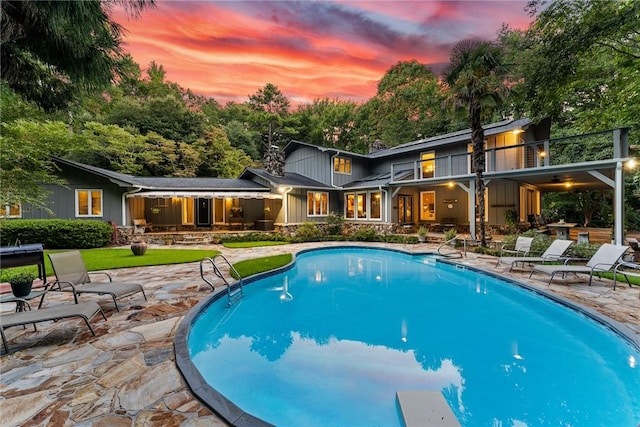 pool at dusk with a patio area and an outdoor pool