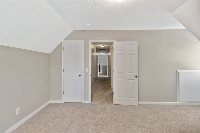 additional living space with a textured ceiling, lofted ceiling, and light carpet