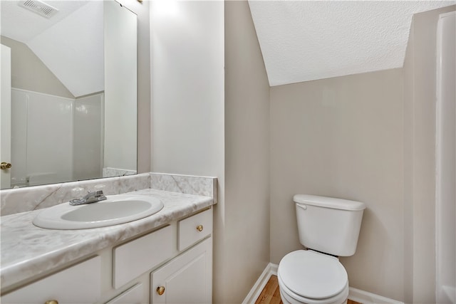 bathroom with a textured ceiling, lofted ceiling, hardwood / wood-style floors, vanity, and toilet