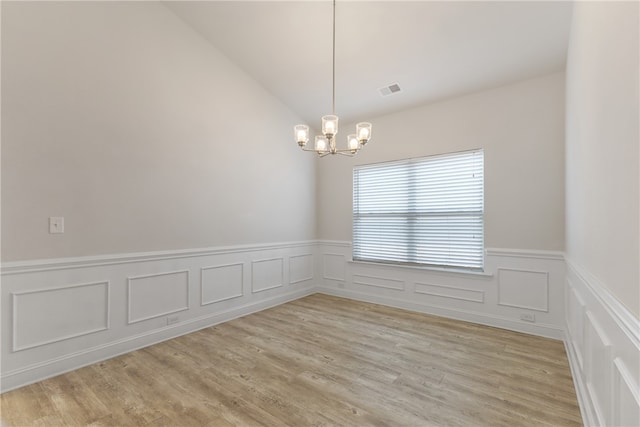 empty room featuring light hardwood / wood-style flooring, a chandelier, and lofted ceiling