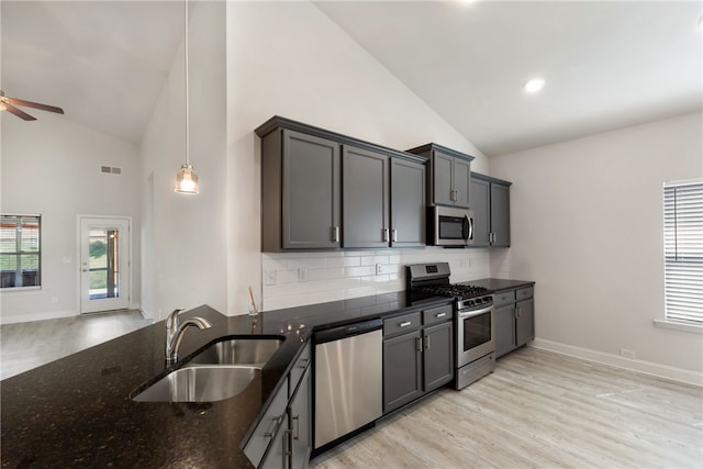 kitchen featuring appliances with stainless steel finishes, pendant lighting, light hardwood / wood-style flooring, dark stone counters, and sink