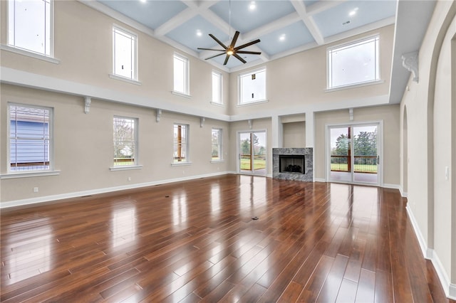 unfurnished living room featuring ceiling fan, a premium fireplace, coffered ceiling, dark hardwood / wood-style floors, and a high ceiling