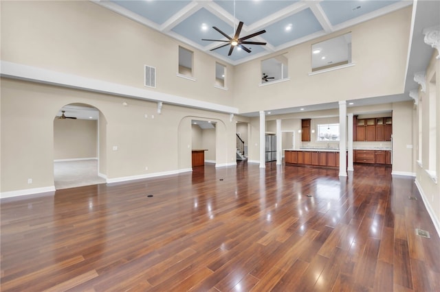 unfurnished living room featuring beamed ceiling, coffered ceiling, a towering ceiling, dark hardwood / wood-style flooring, and ceiling fan