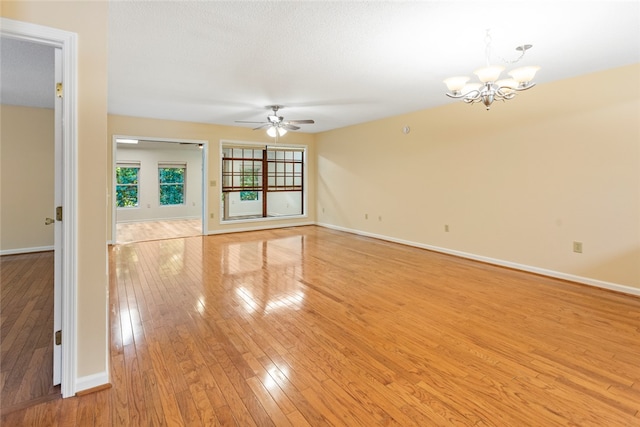 empty room featuring ceiling fan with notable chandelier, light wood-type flooring, and a textured ceiling