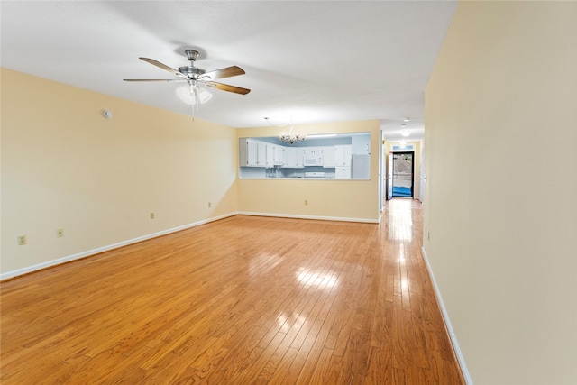 spare room featuring ceiling fan with notable chandelier and light wood-type flooring