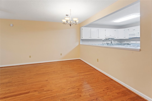 interior space with pendant lighting, light hardwood / wood-style floors, a notable chandelier, white cabinets, and white appliances